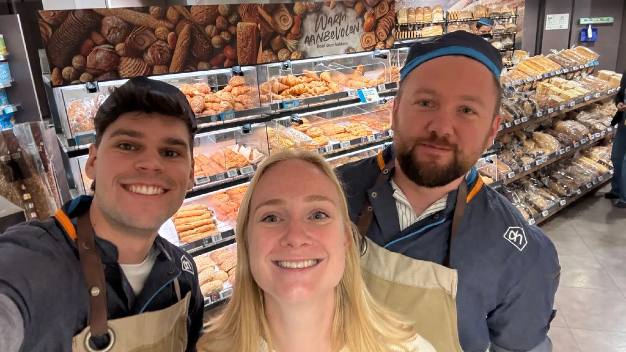 A selfie of me with two bakery colleagues in Albert Heijn uniforms in front of the bread shelves
